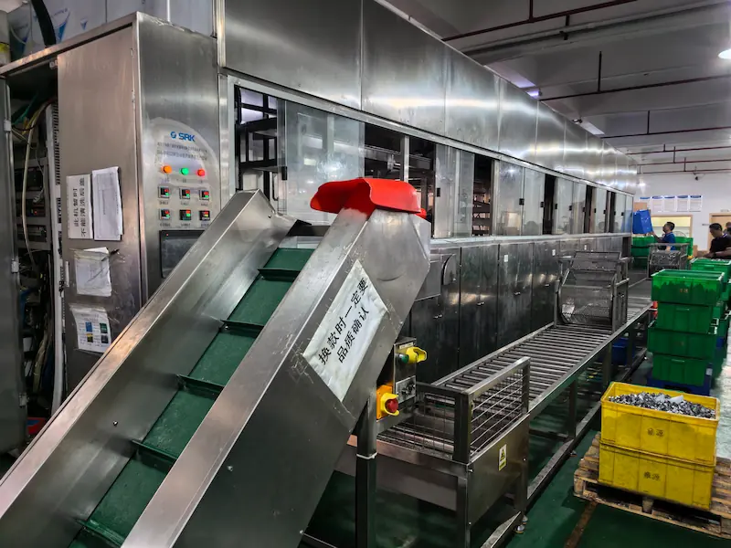 Deep drawn metal components undergoing final edge trimming, ultrasonic cleaning, and surface treatment.